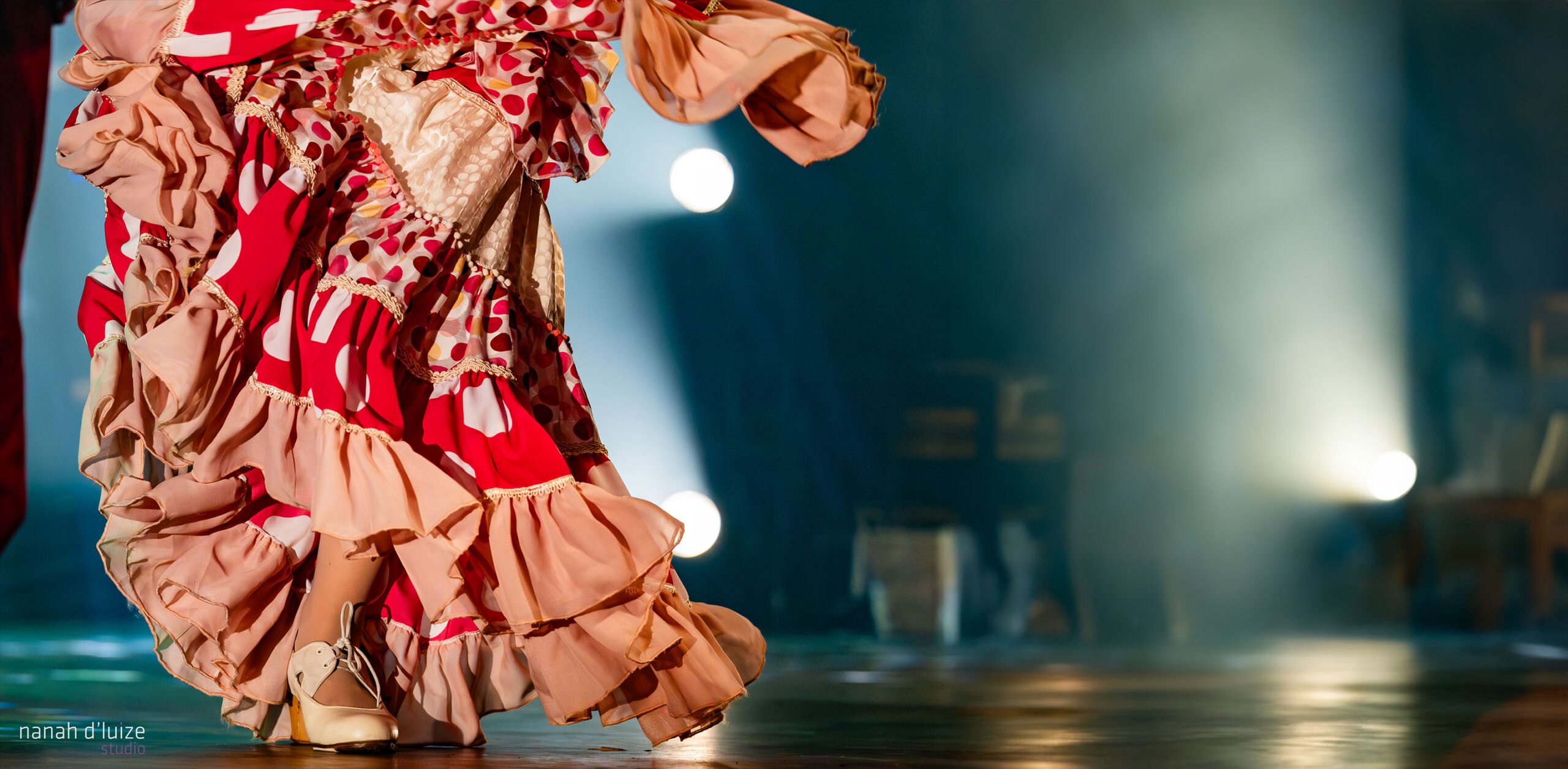 Foto da cintura para baixo de dma dançaria de flamenco em movimento, usando um vestido vermelho e rosa com babados.